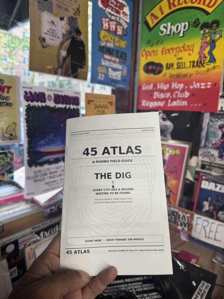 Barry Cole holding the 45 Atlas: The Dig guide inside a record store filled with posters, records, and local music culture