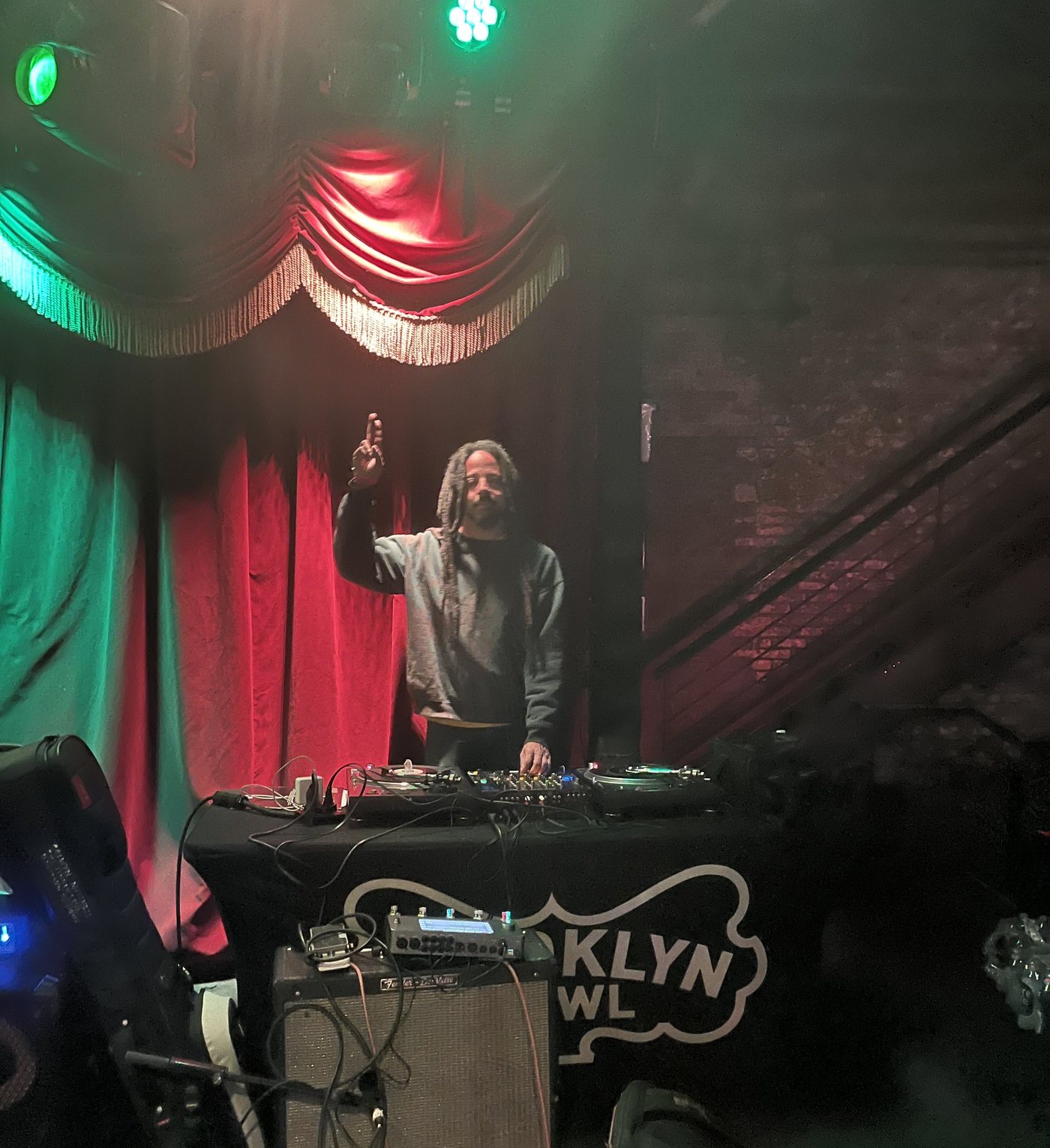 Barry Cole performing behind turntables under red and green stage lighting at Brooklyn Bowl